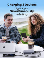 Two people sitting outdoors with a device charging three devices, including a laptop and smartphones.