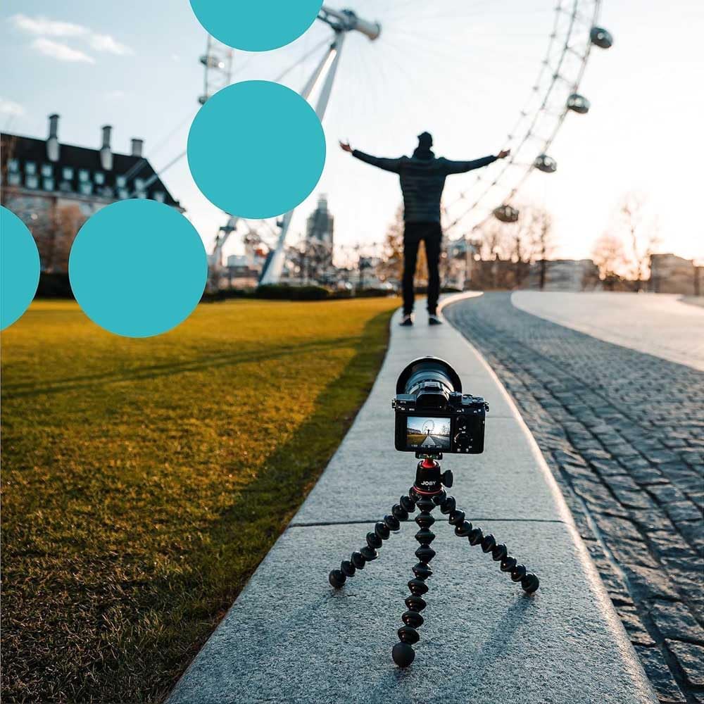 Camera on a tripod with a person standing in front of a Ferris wheel, with blue circles overlayed.