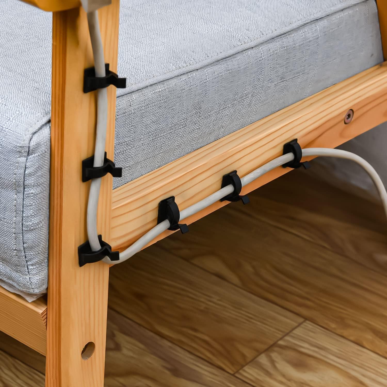 Wooden bed frame with gray mattress and cable management system on a wooden floor.