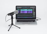 Laptop with audio editing software open, connected to a microphone on a stand.