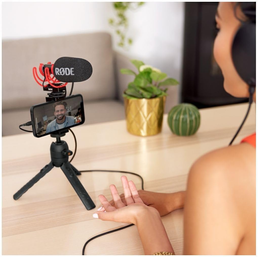 Person using a smartphone with a RODE microphone on a tripod, sitting on a couch.
